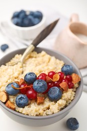 Photo of Bowl of delicious cooked quinoa with almonds, cranberries and blueberries on white table, closeup