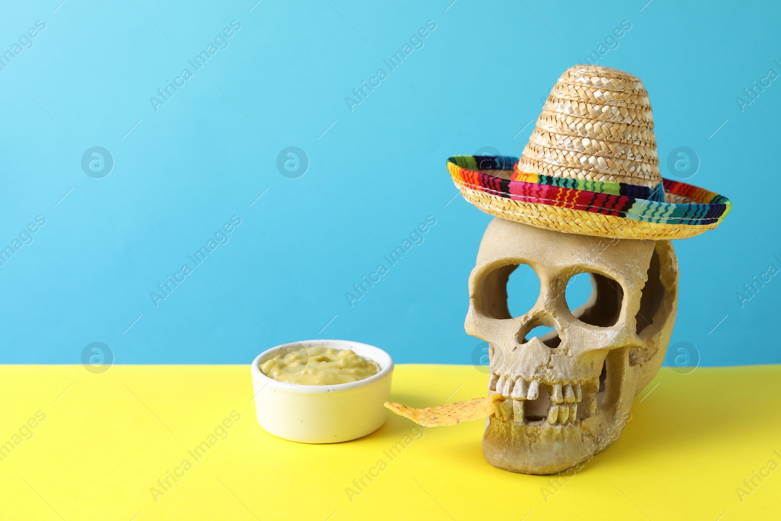 Photo of Human scull with Mexican sombrero hat, nachos chip and guacamole on color background. Space for text