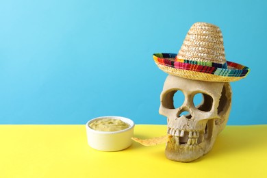Human scull with Mexican sombrero hat, nachos chip and guacamole on color background. Space for text