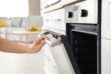 Photo of Woman opening door of oven in kitchen, closeup