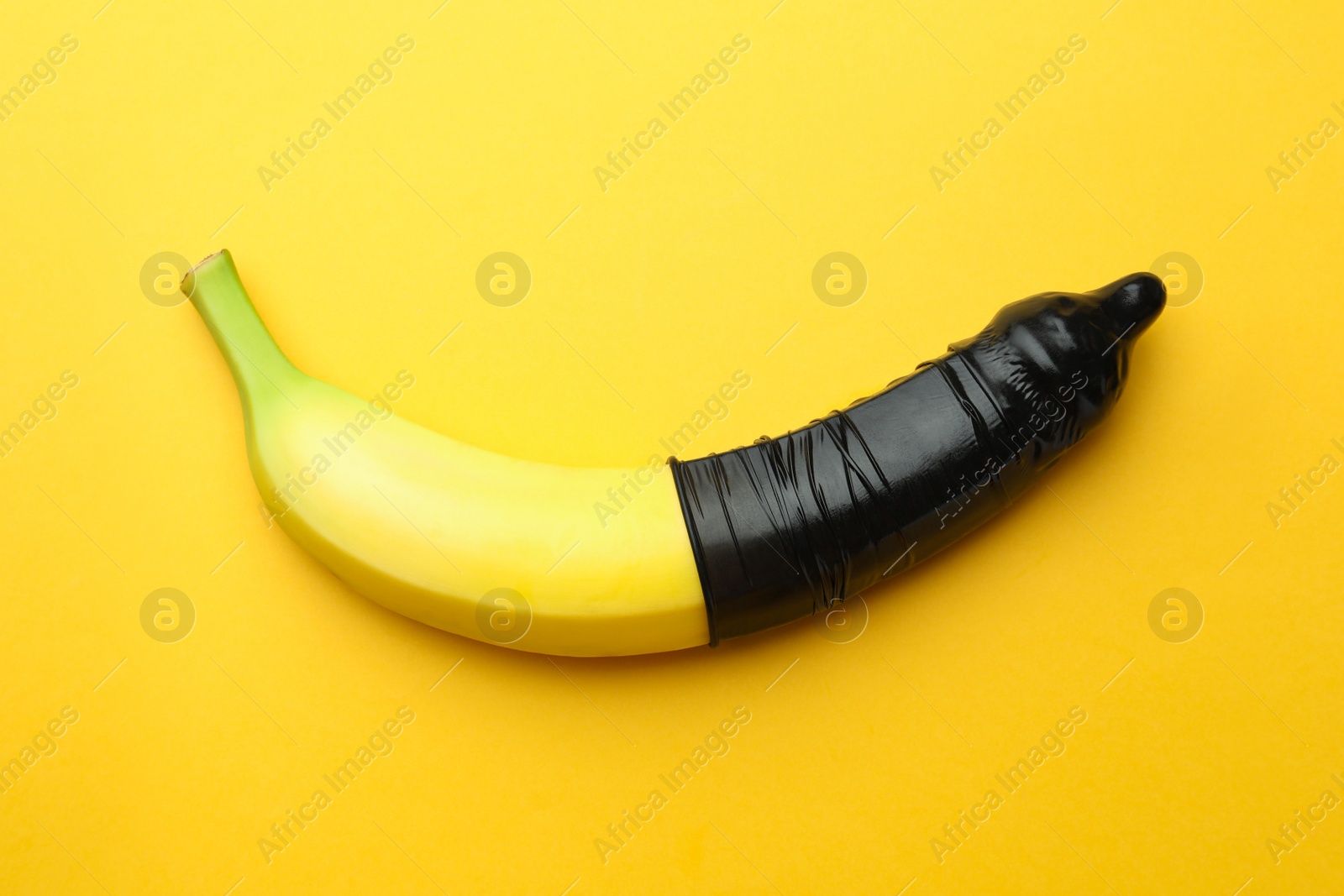 Photo of Banana with condom on orange background, top view. Safe sex concept