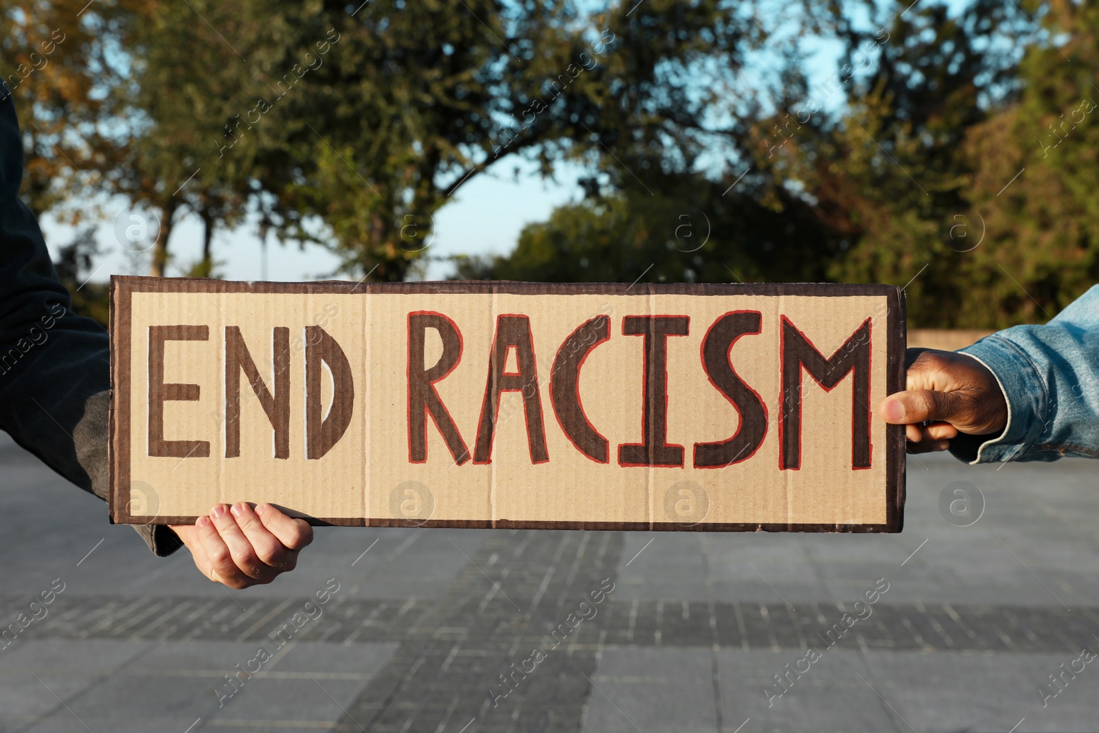 Photo of Men holding sign with phrase End Racism outdoors, closeup