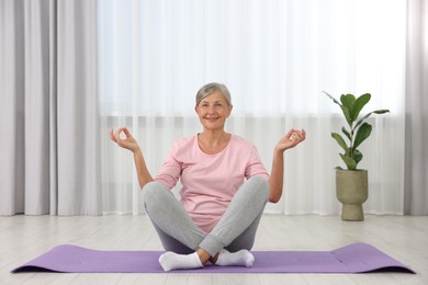 Photo of Happy senior woman practicing yoga on mat at home