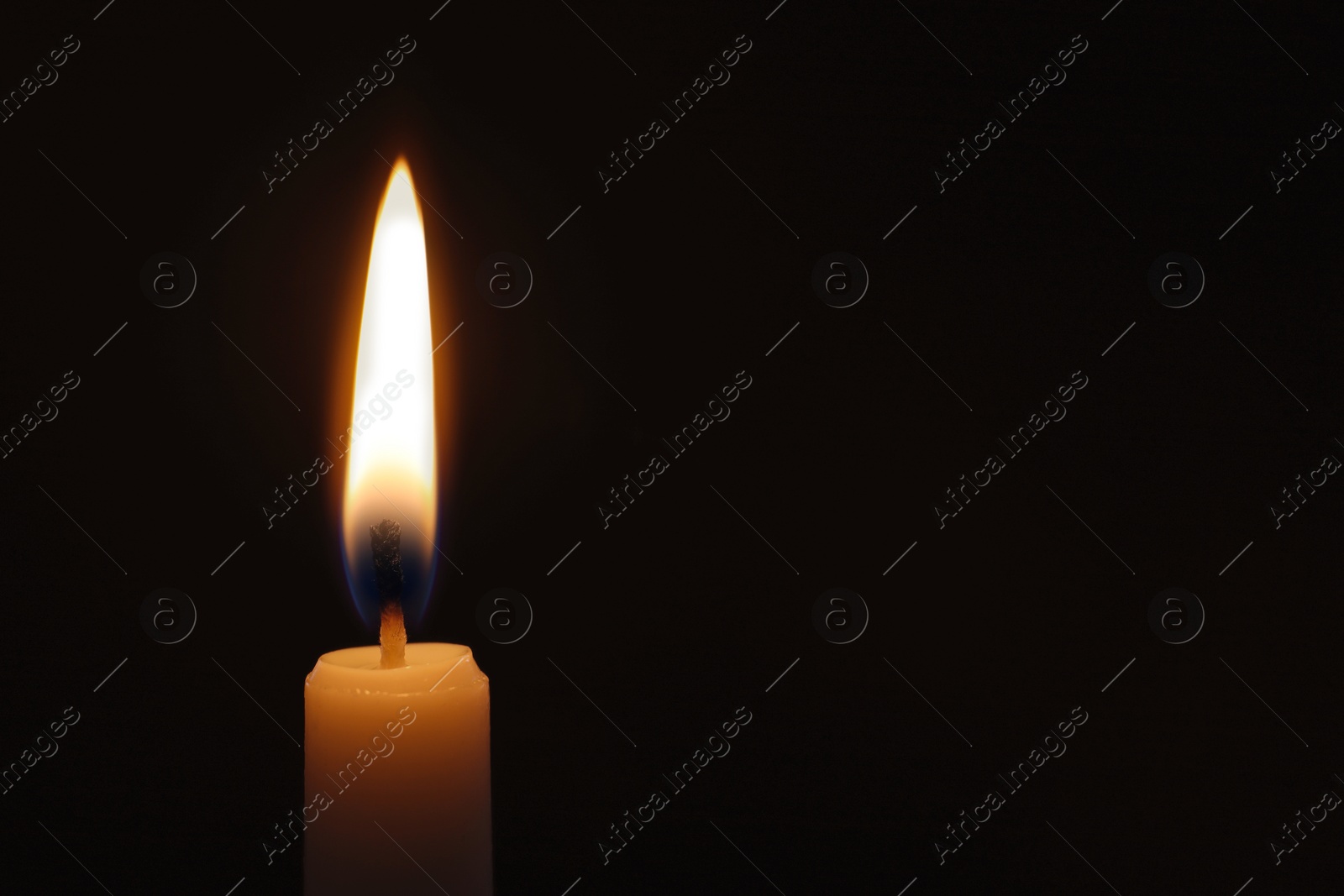 Photo of Wax candle burning on black background, closeup