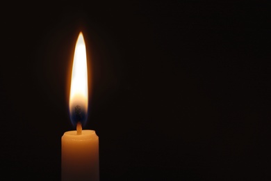 Photo of Wax candle burning on black background, closeup