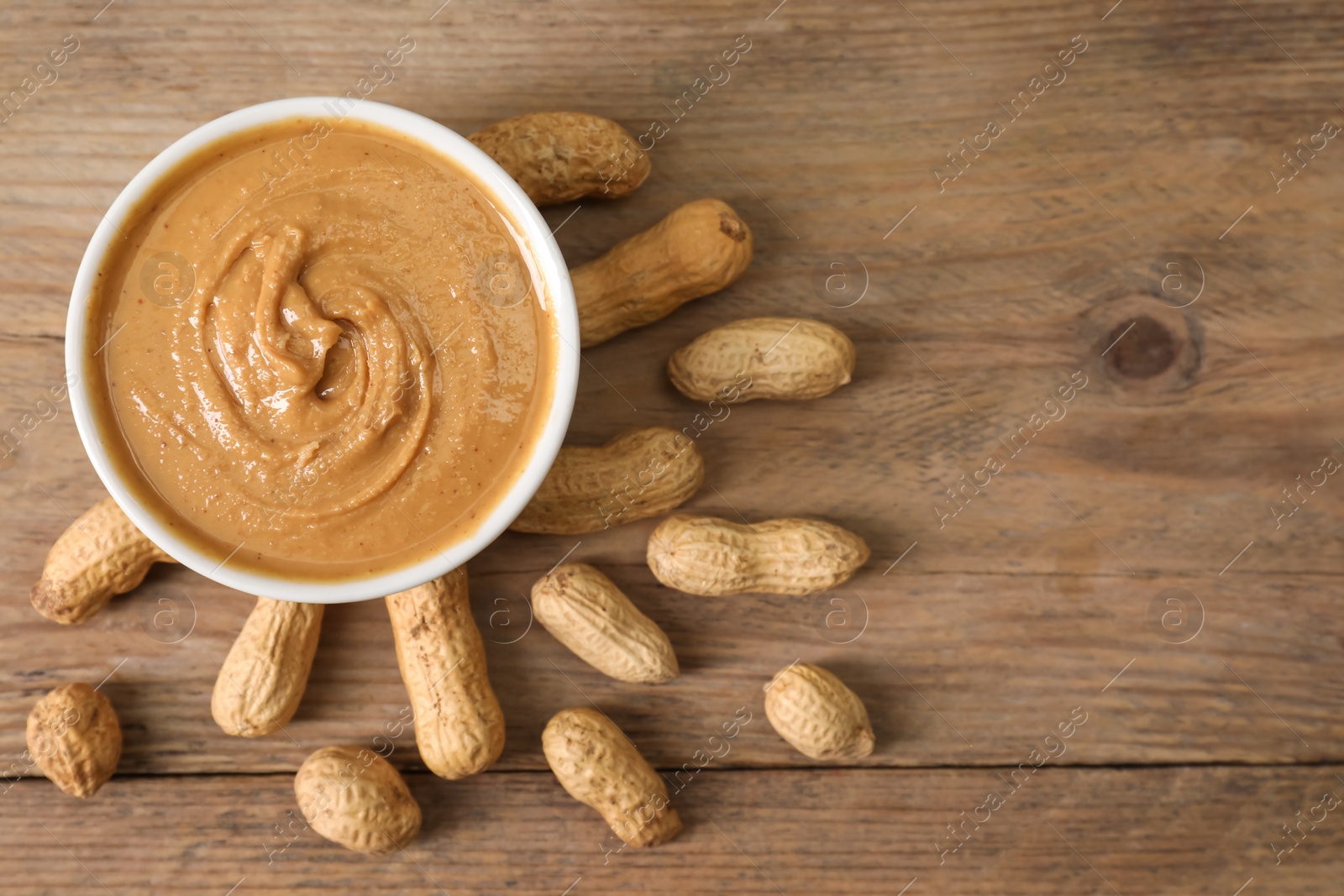 Photo of Delicious nut butter in bowl and peanuts on wooden table, top view. Space for text