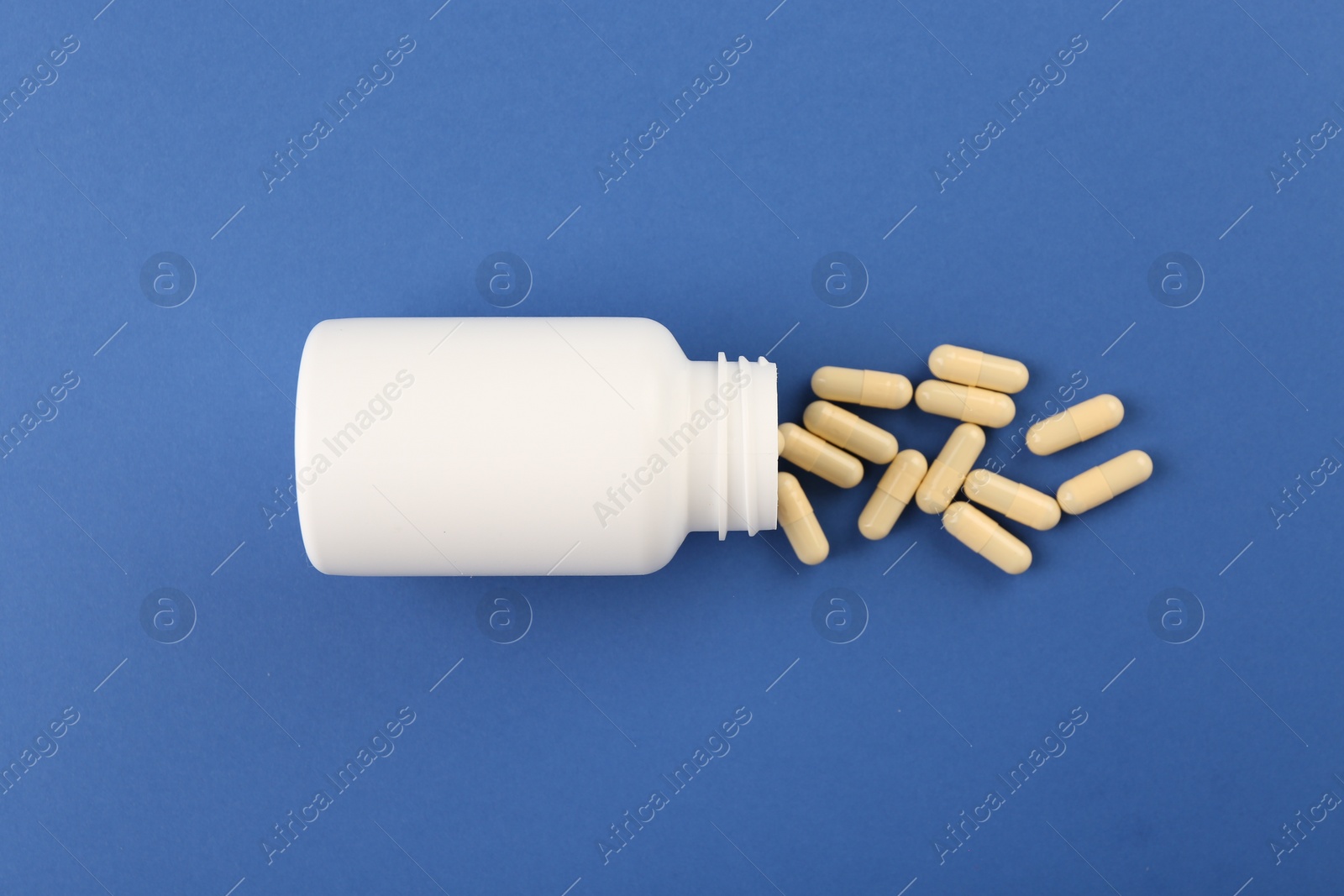 Photo of Bottle and vitamin capsules on blue background, top view