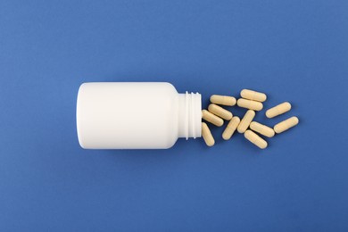 Bottle and vitamin capsules on blue background, top view