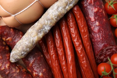 Different types of tasty sausages and tomatoes as background, top view