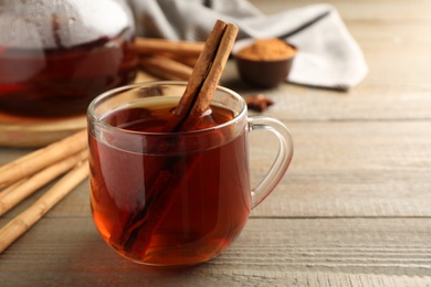 Photo of Glass cup of hot tea with aromatic cinnamon on wooden table. Space for text