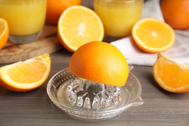 Photo of Fresh ripe oranges and glass squeezer on wooden table