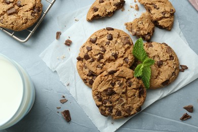 Photo of Tasty chocolate chip cookies, glass of milk and mint leaves on light grey table, flat lay