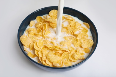 Photo of Milk pouring into bowl with crispy cornflakes on white background