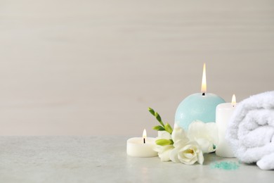 Photo of Beautiful spa composition with burning candle, rolled towel and flowers on white table. Space for text