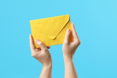 Woman holding yellow paper envelope on light blue background, closeup