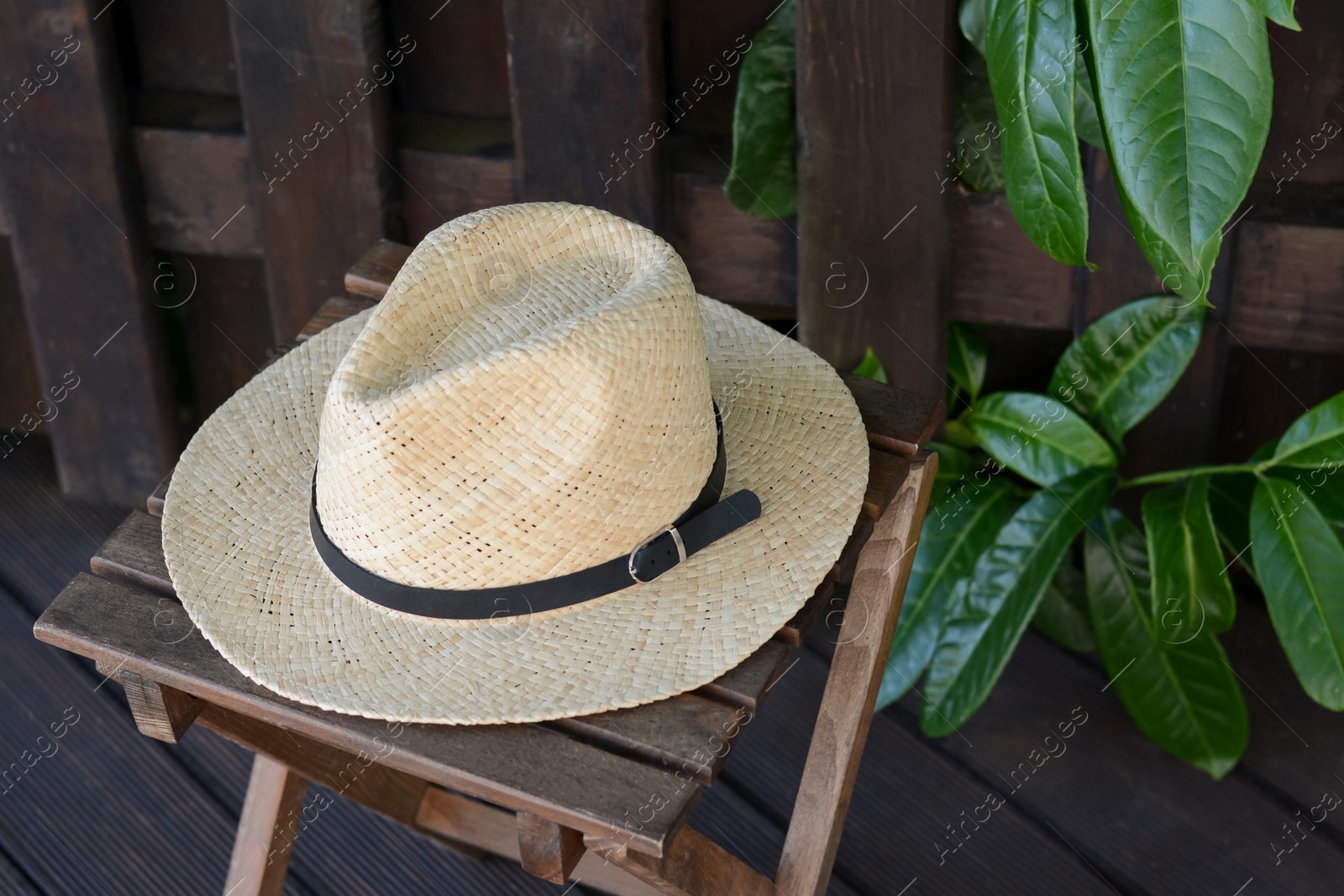 Photo of Stylish hat on wooden stool near fence. Beach accessory