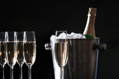 Photo of Glasses with champagne and bottle in bucket against dark background