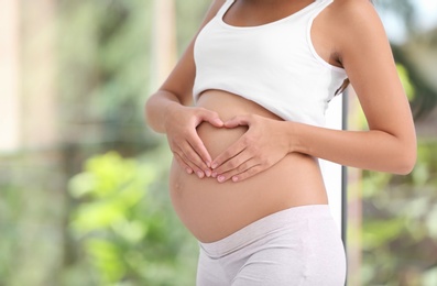 Photo of Pregnant woman standing near window at home, closeup