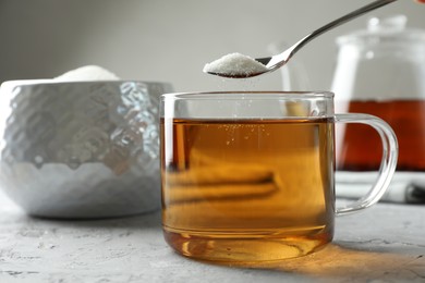 Photo of Adding sugar into cup of tea at grey textured table, closeup
