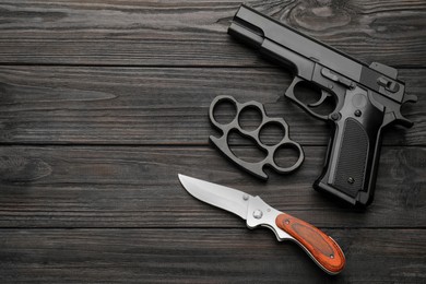 Photo of Brass knuckles, gun and knife on black wooden background, flat lay. Space for text
