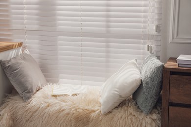 Photo of Comfortable place for relax with faux fur and pillows near window in room