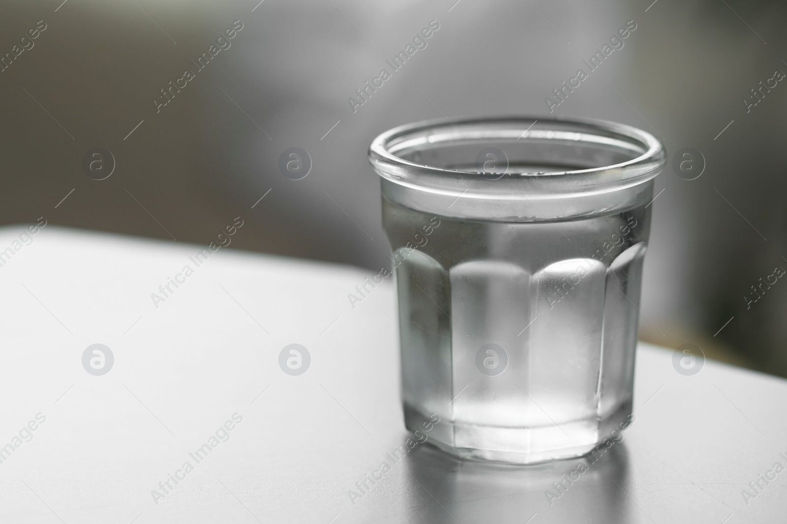 Photo of Glass of pure water on light table against blurred background, space for text