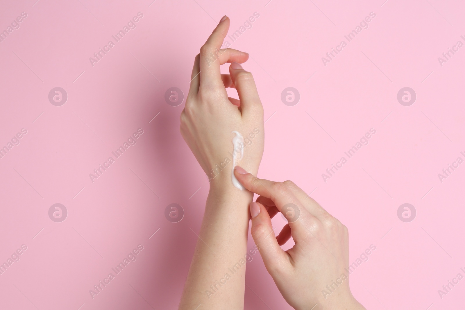 Photo of Woman applying cream on her hand against pink background, closeup