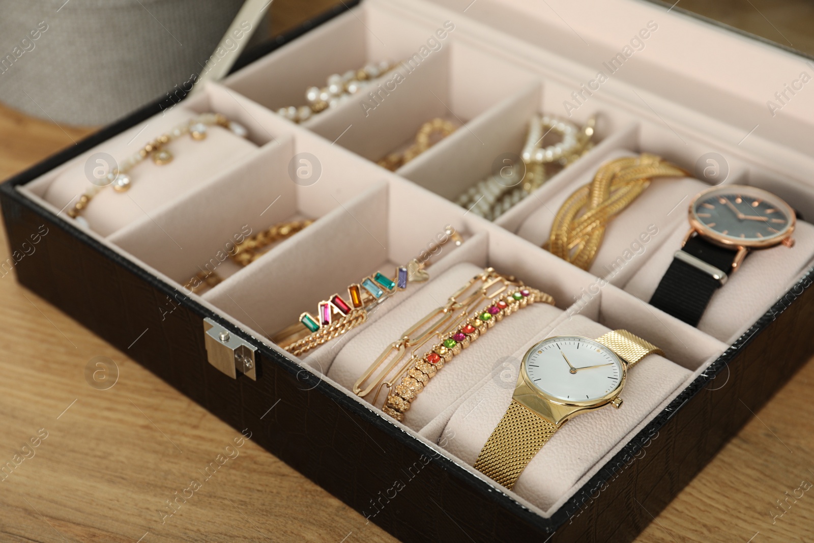 Photo of Elegant jewelry box with beautiful bijouterie and expensive wristwatches on wooden table, closeup