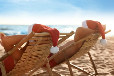 Photo of Lovely couple with Santa hats relaxing on deck chairs at beach. Christmas vacation