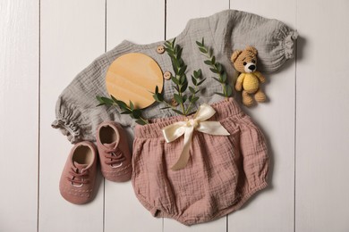 Flat lay composition with children's clothes, shoes and toy on white wooden table