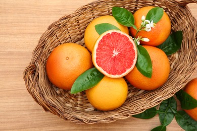 Photo of Wicker basket with fresh ripe grapefruits and green leaves on wooden table, top view