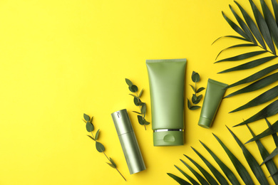 Photo of Set of cosmetic products and green leaves on yellow background, flat lay