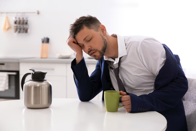 Sleepy man with cup of drink at home in morning