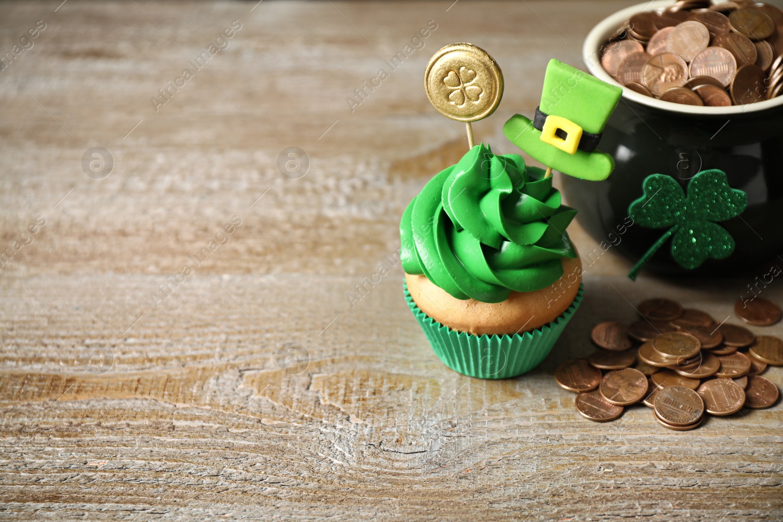 Photo of Decorated cupcake and pot with gold coins on wooden table, space for text. St. Patrick's Day celebration