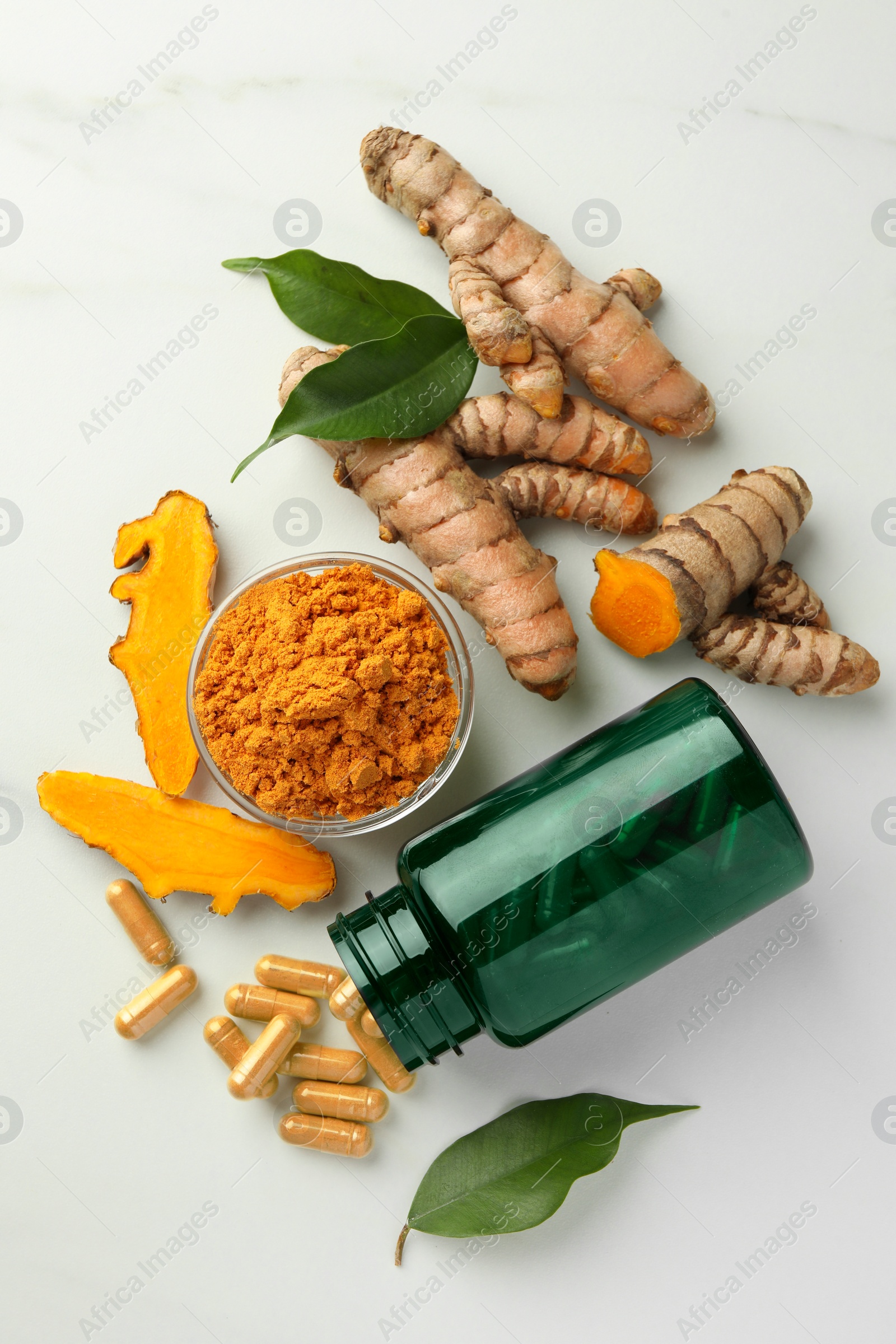 Photo of Aromatic turmeric powder, pills and raw roots on white marble table, flat lay