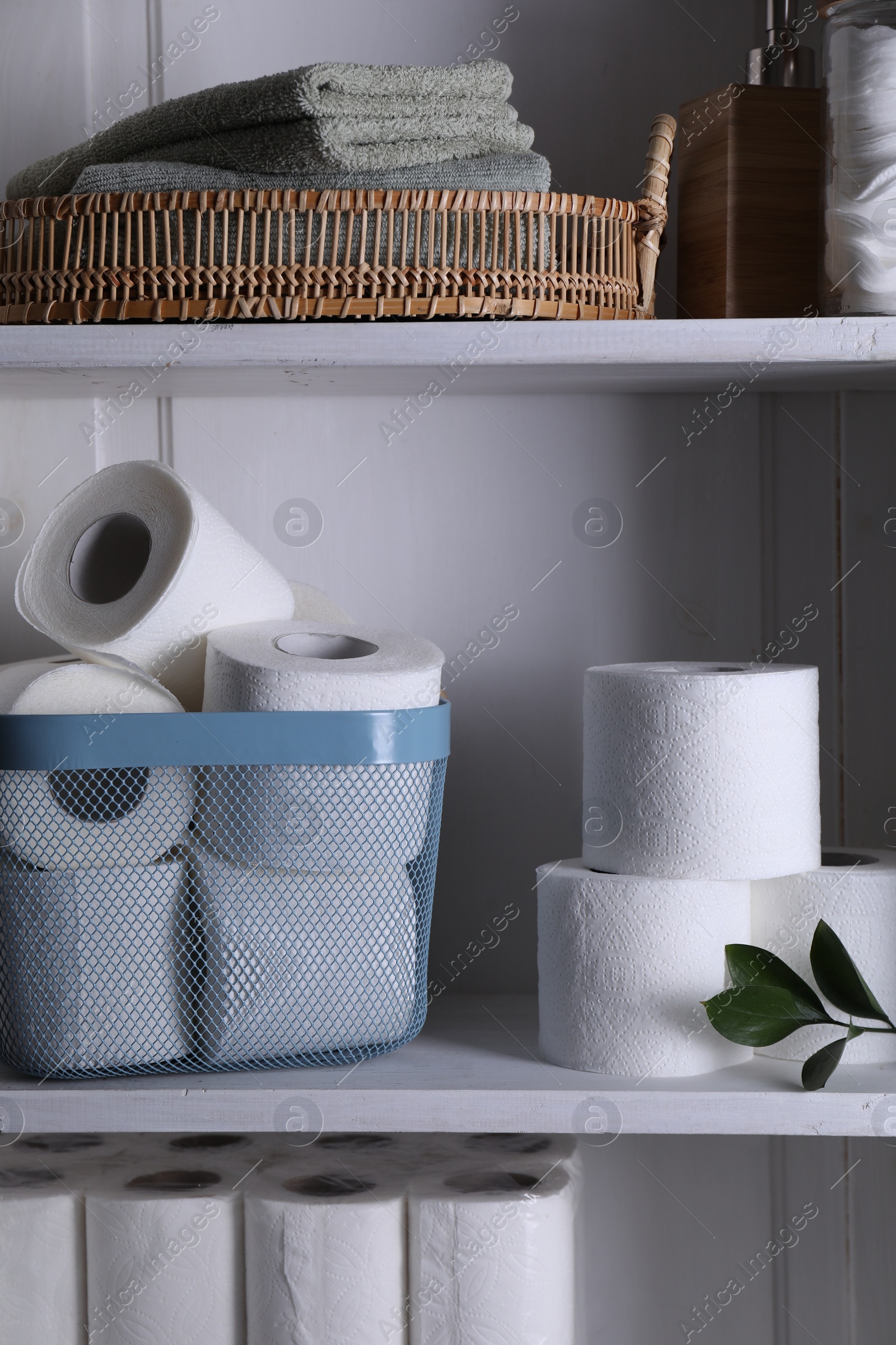 Photo of Toilet paper rolls, green leaves and towels on white shelves