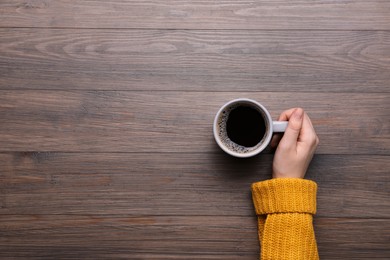 Photo of Woman with cup of coffee at wooden table, top view. Space for text