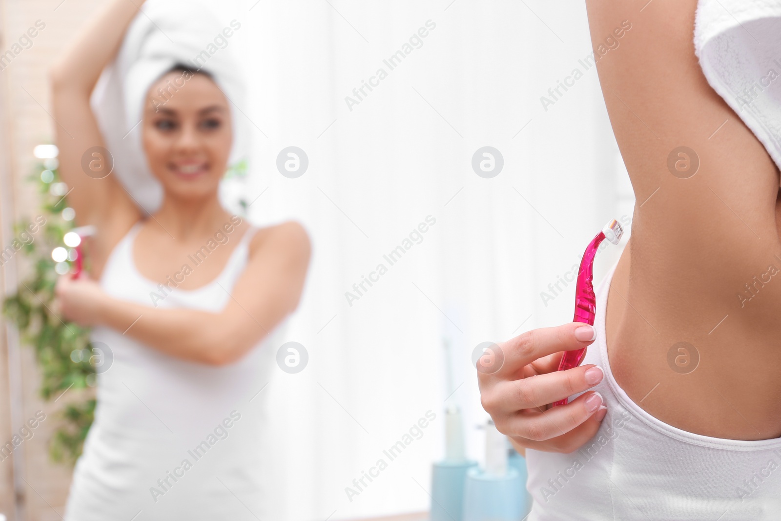 Photo of Beautiful young woman shaving armpit at home