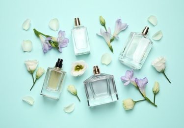 Photo of Flat lay composition with different perfume bottles and flowers on cyan background
