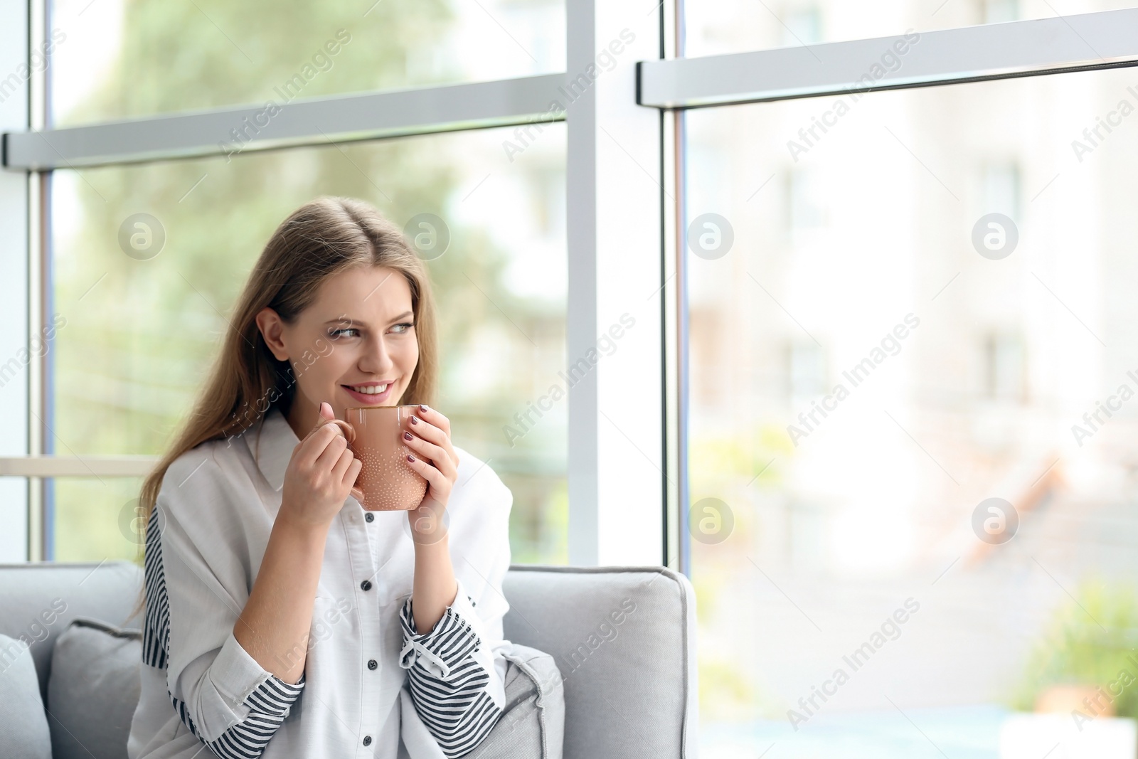 Photo of Young beautiful woman drinking morning coffee near window at home