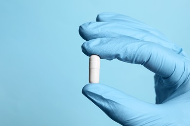 Photo of Doctor holding pill on light blue background, closeup. Space for text