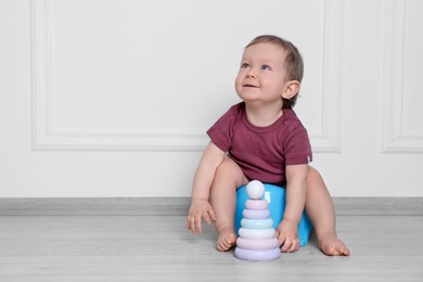 Photo of Little child with toy pyramid sitting on baby potty near white wall. Space for text