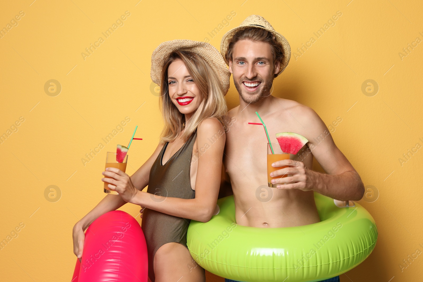 Photo of Happy young couple in beachwear with inflatable rings and cocktails on color background