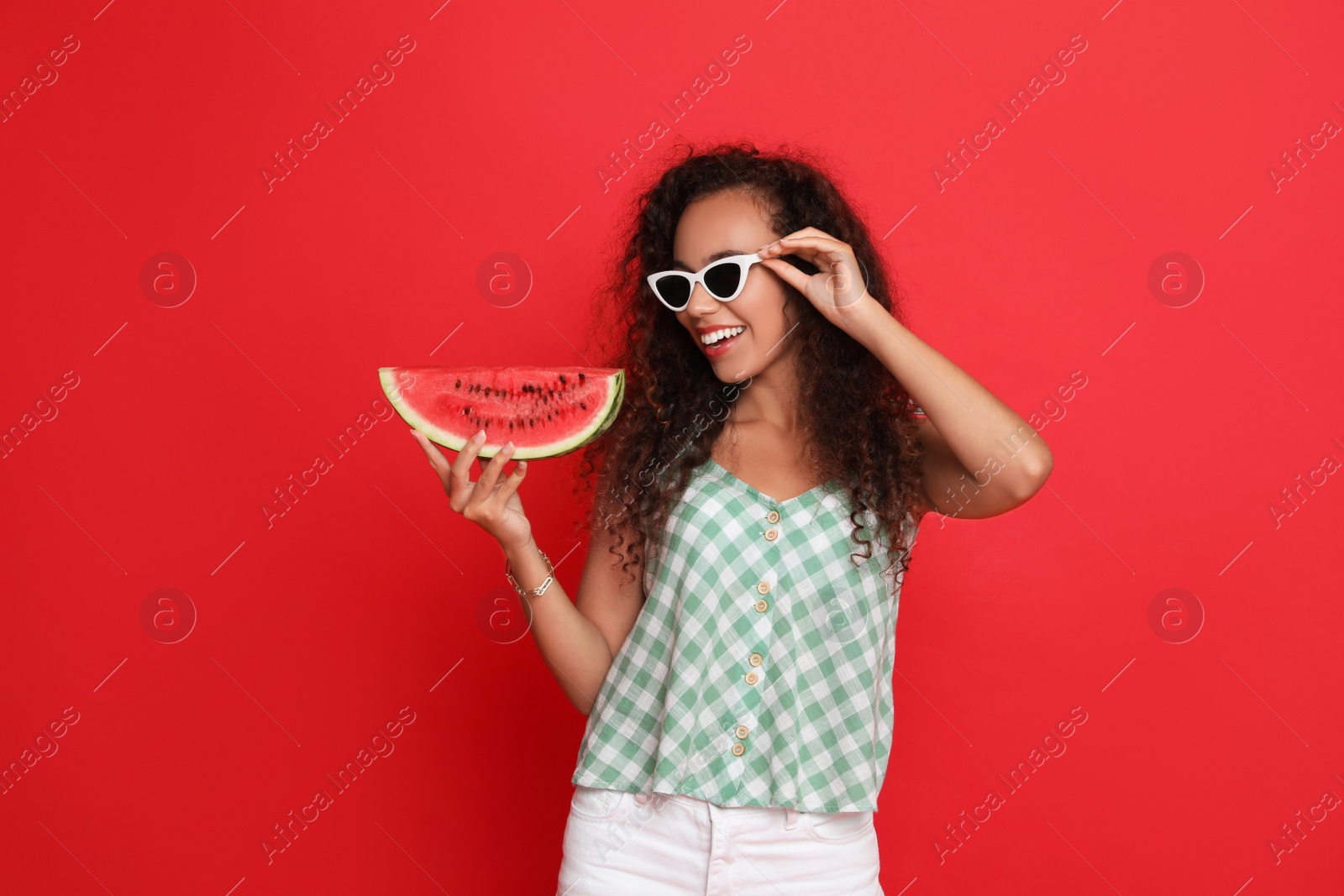 Photo of Beautiful young African American woman with slice of watermelon on red background