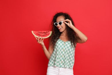 Photo of Beautiful young African American woman with slice of watermelon on red background