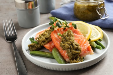 Photo of Tasty cooked salmon with pesto sauce served on grey table