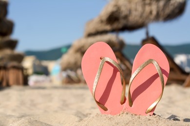 Photo of Stylish flip flops in sand on beach, space for text