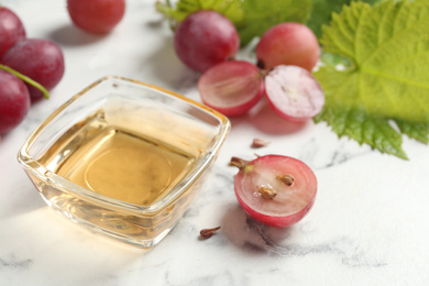 Photo of Bowl of natural grape seed oil on white marble table. Organic cosmetic