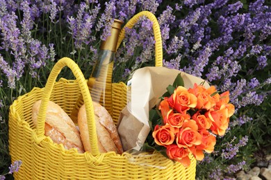 Photo of Yellow wicker bag with beautiful roses, bottle of wine and baguettes in lavender field