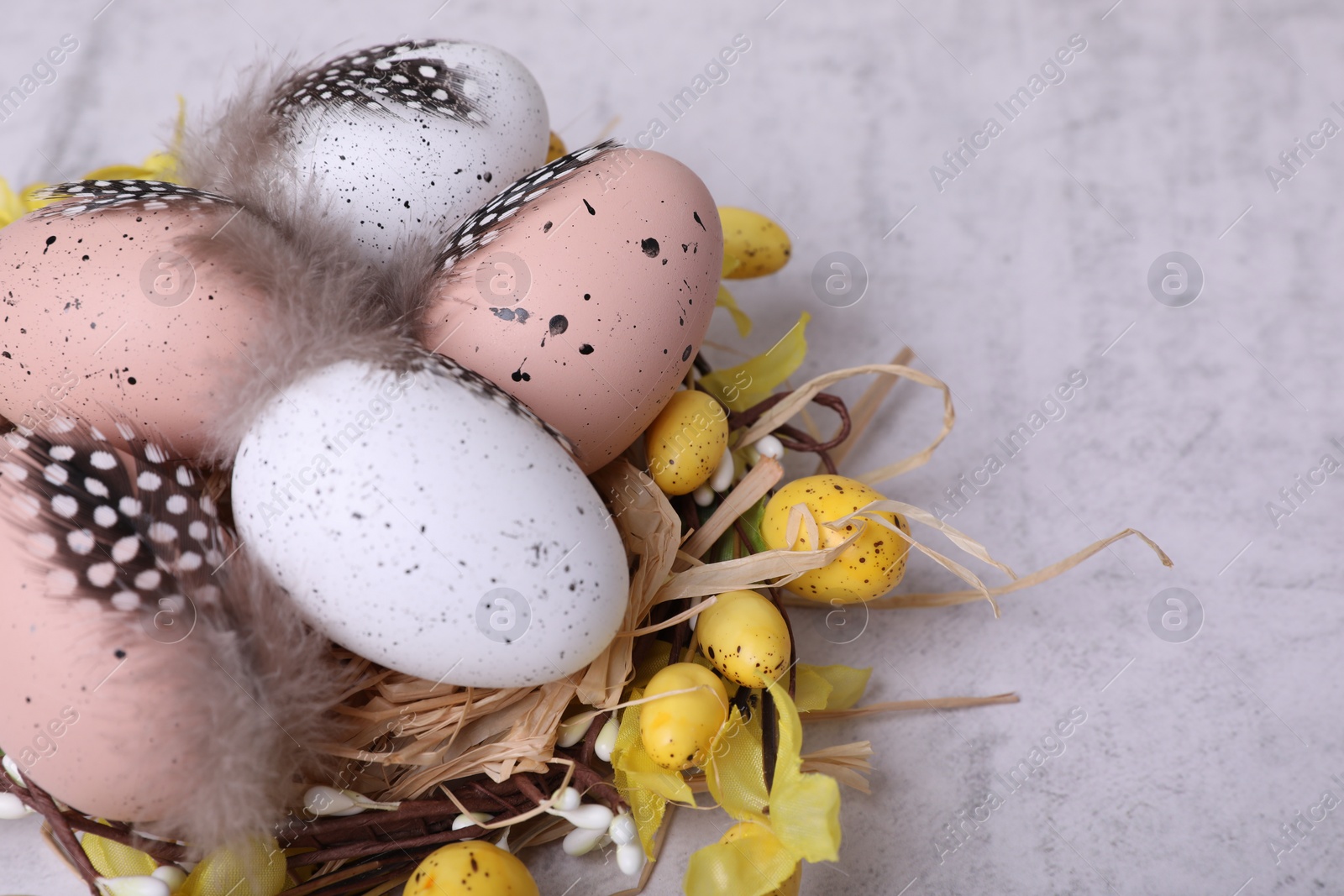 Photo of Decorative nest with many painted Easter eggs on light textured background, closeup. Space for text